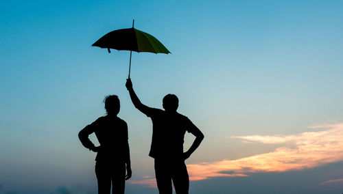 Silhouette man with woman holding umbrella against sky during sunset