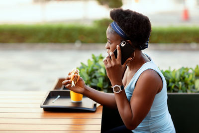 Cute african woman having lunch outdoors in city cafe. a girl is talking on the phone during lunch