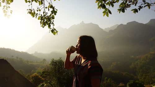 Woman drinking coffee by mountains against sky
