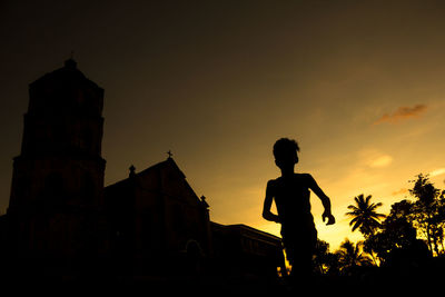 Silhouette man standing by building against sky during sunset