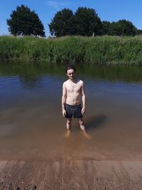 Full length of shirtless man standing on lake against trees