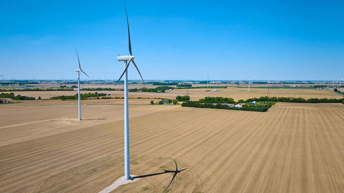 Windmills on field against clear blue sky