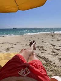 Low section of person lying on beach against sky