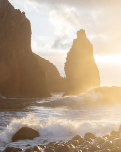 Scenic view of waves in sea by rocks against sky