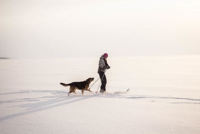 View of woman walking with dog on snow covered beach
