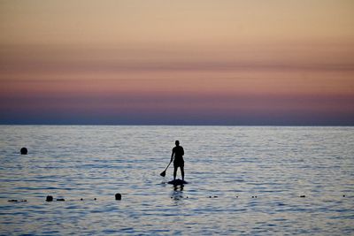 Silhouette man standing in sea against sky during sunset