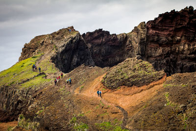 Low angle view of hikers walking on mountain against sky