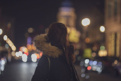 Portrait of young woman standing on illuminated street at night