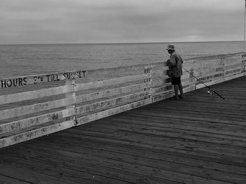 Rear view of man standing on railing against sea