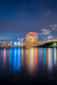 Illuminated ferris wheel by sea against sky at night