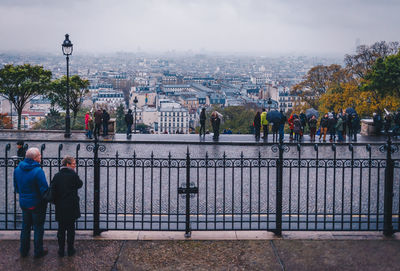 Rear view of people standing by railing in city