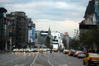 Cars on city street by buildings against sky