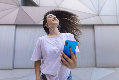 Young woman dancing on the street with headphones while moving her hair