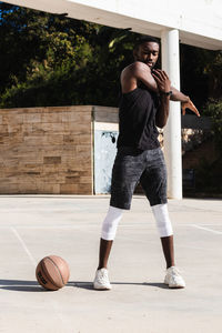 Fit african american male basketball player warming up stretching while preparing for training on sports grond in summer with eyes closed