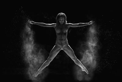 Full length of muscular woman jumping against black background