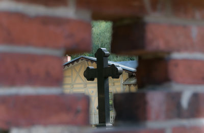 Cross seen through hole on brick wall