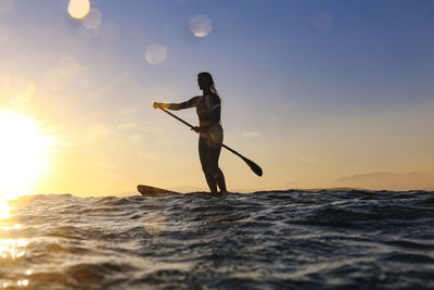 Silhouette man standing in sea against sky during sunset