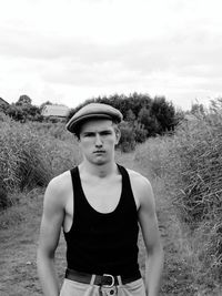 Portrait of young man standing on field against sky