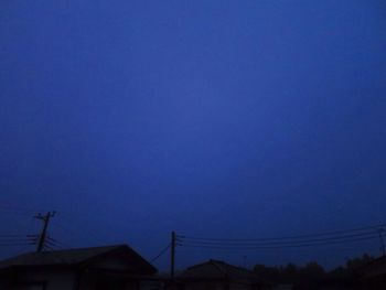 Low angle view of silhouette electricity pylon against blue sky