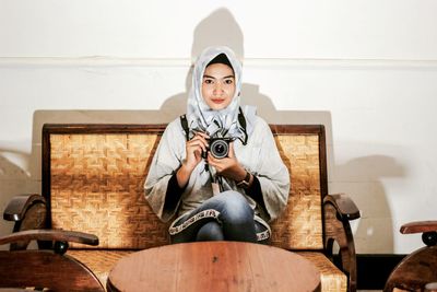 Portrait of woman photographing while sitting on sofa at home