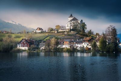 Buildings by river against sky