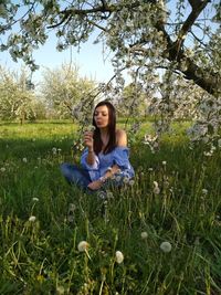 Young woman sitting with dandelion seed on field at park