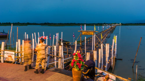 Soldiers standing by bamboo bridge and phayao lake against sky at dusk