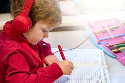 Side view of girl wearing headphones writing in book