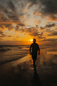 Silhouette man standing at beach against sky during sunset