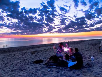 People sitting on beach against sky during sunset