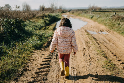 Rear view girl walking on a puddle with rubber boots