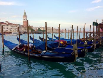 Gondolas moored in canal against sky