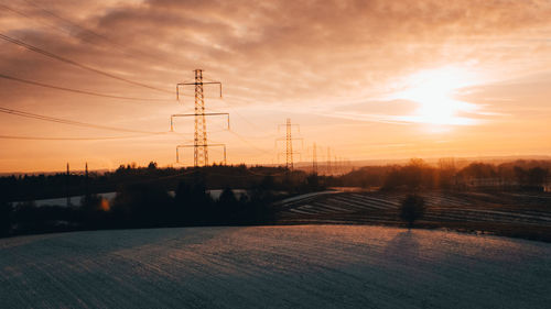 Electricity pylon on field against sky at sunset