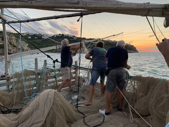 Rear view of people standing by sea against sky during sunset