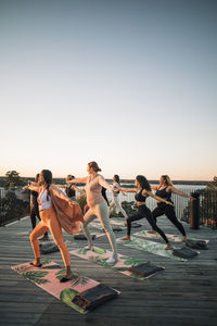 Female friends practicing warrior 2 pose on patio at retreat center