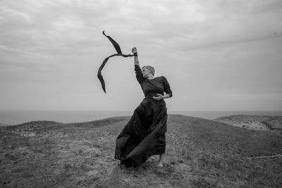 Woman with arms raised dancing on grass against sky