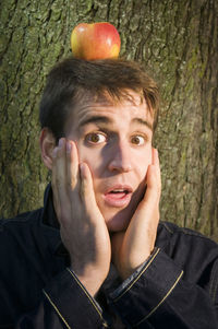 Portrait of mid adult man with apple on head against tree trunk