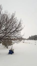 Bare tree on snow covered landscape against clear sky