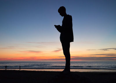 Silhouette man standing on beach against sky during sunset