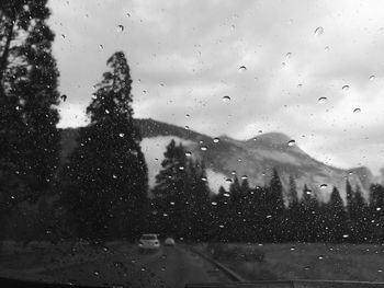 Trees against mountains seen through wet windshield during rainy season