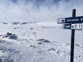 Road sign on snow covered landscape against sky