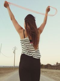 Woman with arms raised standing on beach against clear sky