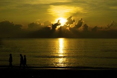 Silhouette people on sea against sky during sunset