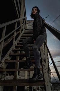 Low angle view of woman sitting on railing against sky