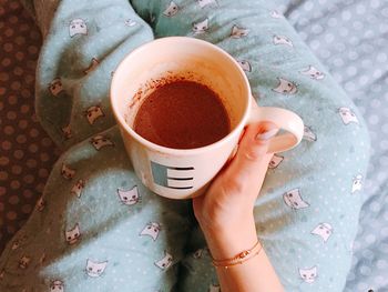 Midsection of woman holding hot chocolate in mug on bed