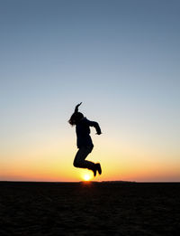 Silhouette woman jumping on beach at sunset