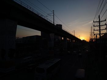 Silhouette bridge against sky during sunset in city