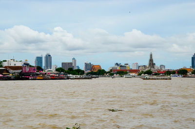 Boats on chao phraya river against cloudy sky