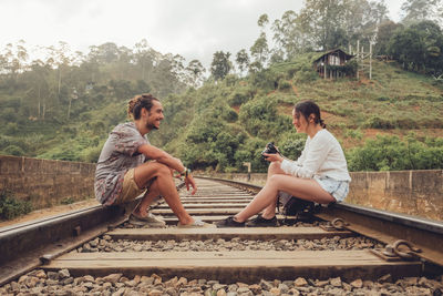 Friends sitting on railroad track by trees