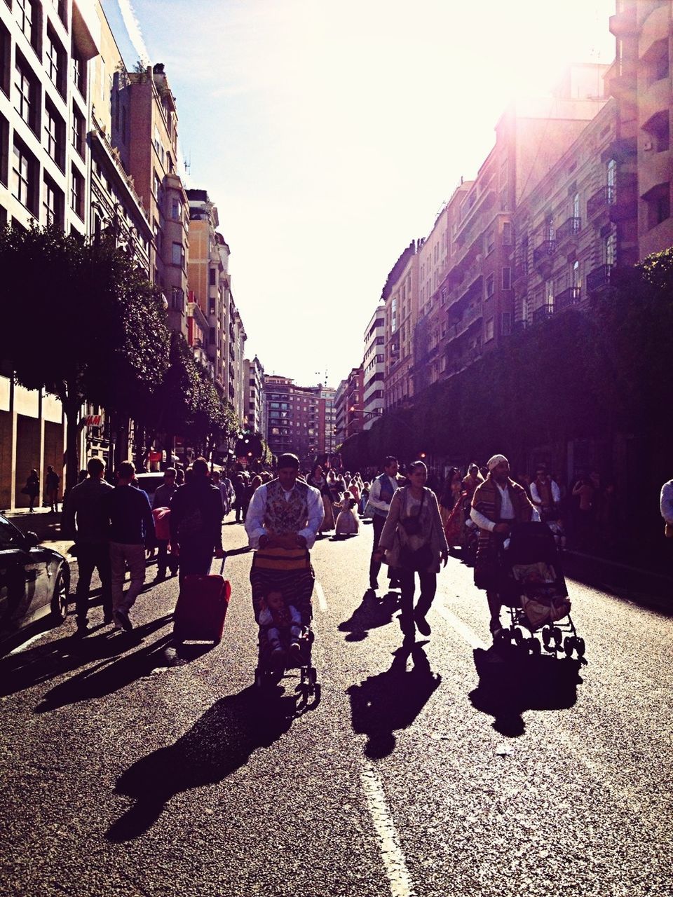 building exterior, architecture, built structure, street, men, city, lifestyles, person, walking, sunlight, city life, leisure activity, large group of people, city street, shadow, road, transportation, outdoors, medium group of people